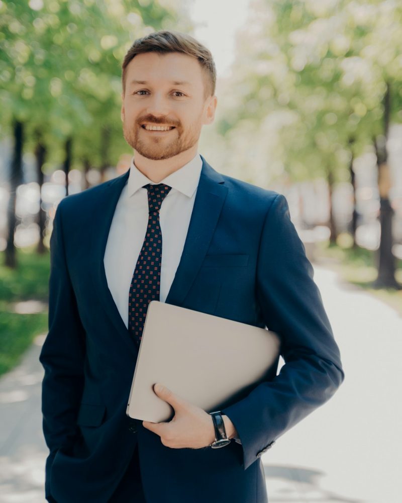 Businessman in suit walking on street holding laptop